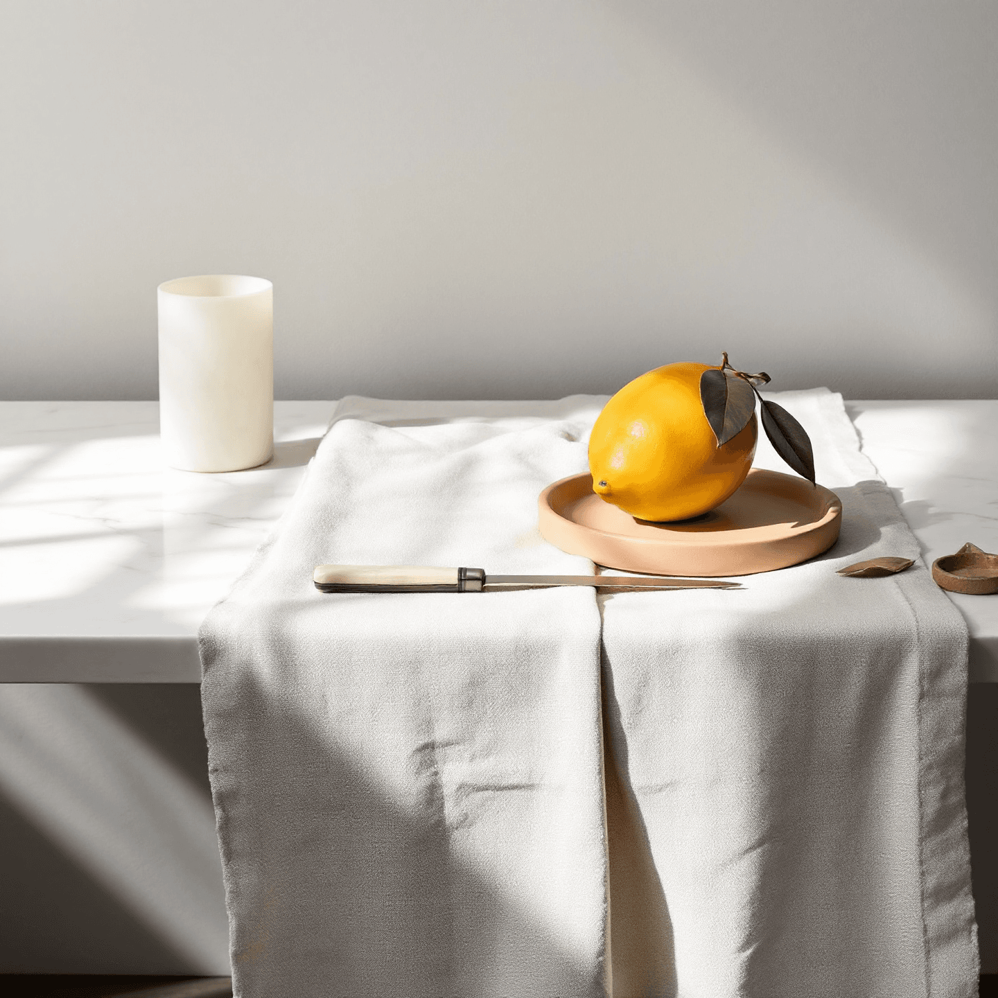 cast bronze lemon with brushed cool patina — on a raw linen runner with terracotta dish and bone-handled knife, late-afternoon side light